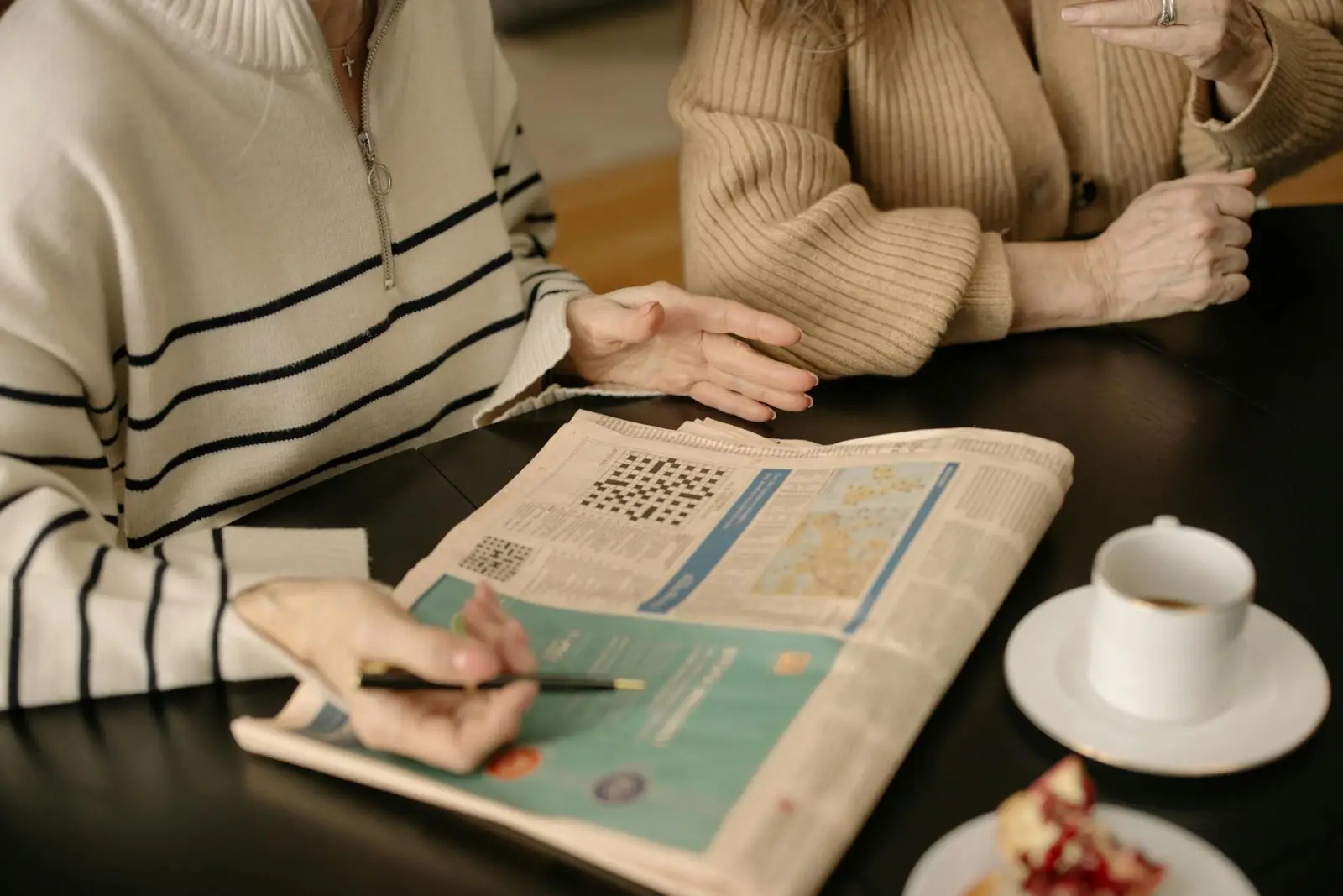 Two older adults reviewing a newspaper and crossword together at a kitchen table
