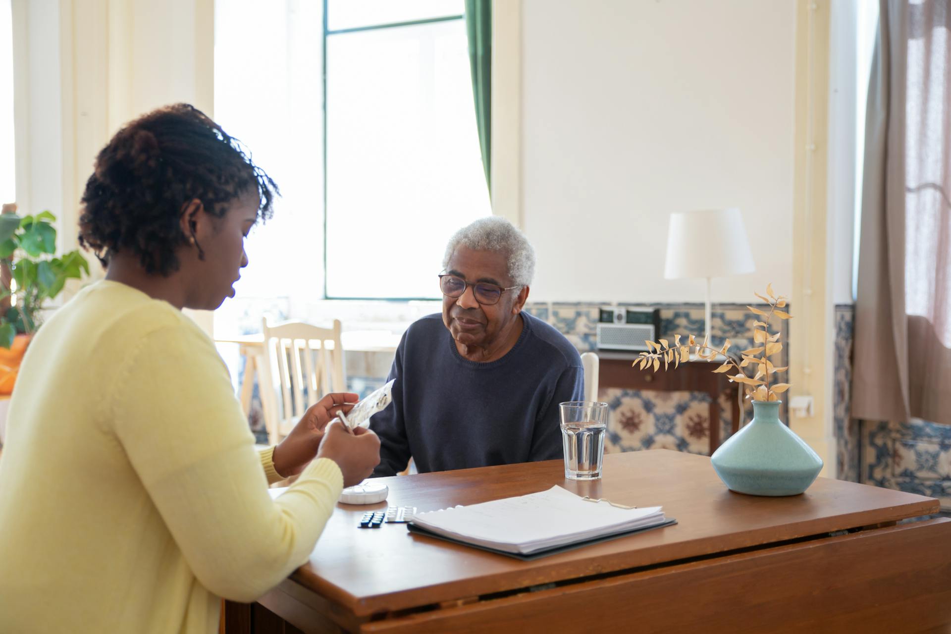 In-home caregiver helping an older adult organize medications and paperwork at a dining table